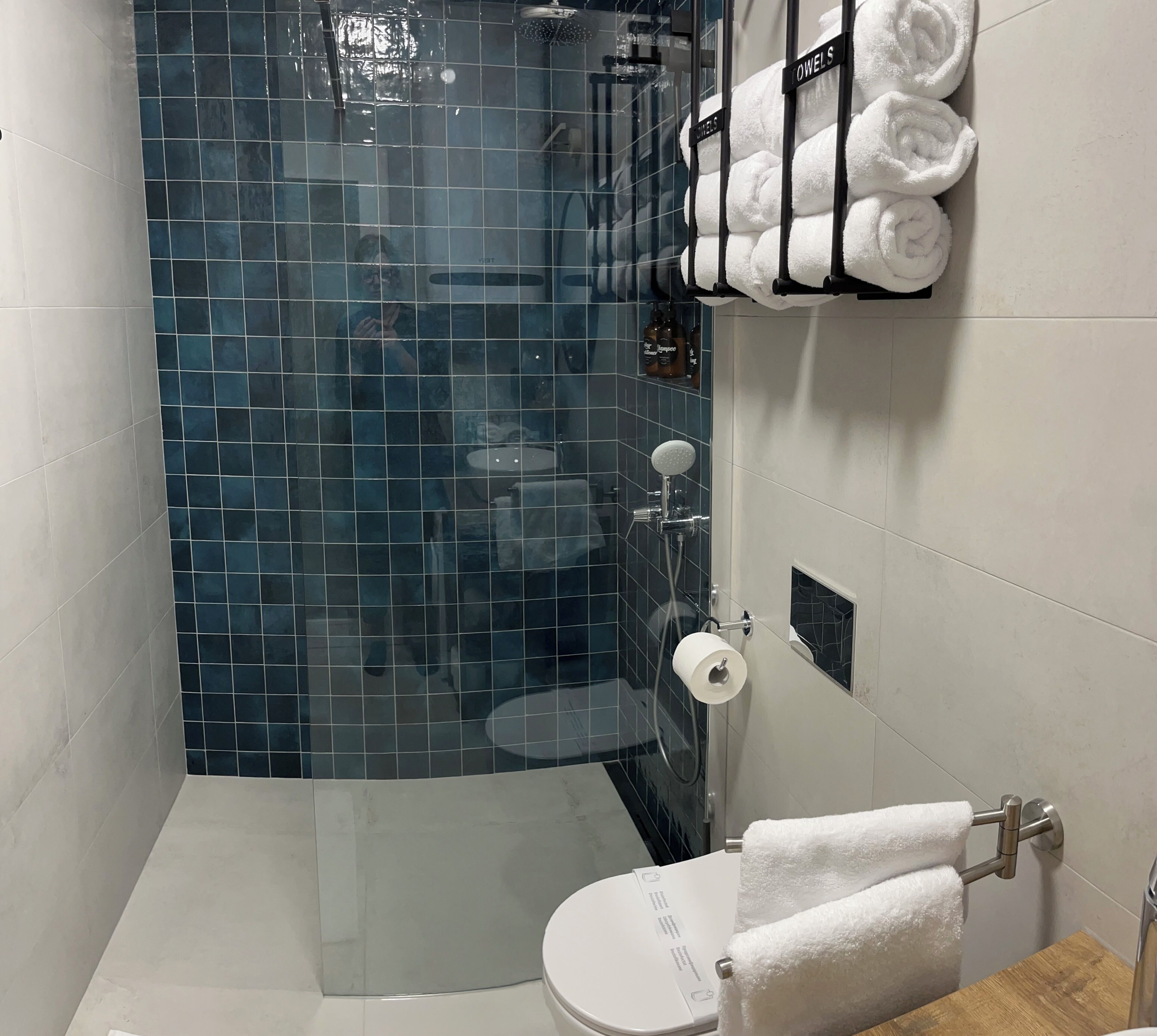 A bathroom with a glass-enclosed shower, a toilet, and a towel rack with folded towels.