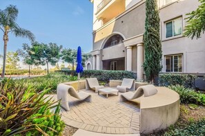 Relax in a serene outdoor space with lounge chairs and a coffee table, surrounded by lush vegetation and a shaded area.