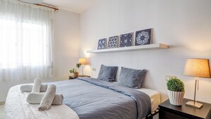 A neatly made bed with towels, a bedside lamp, a small plant, and decorative wall art.