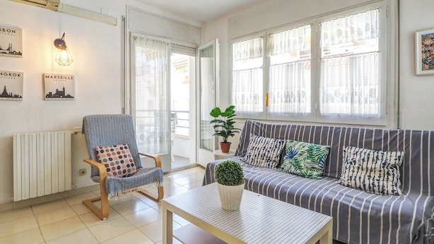A living room with a striped sofa, a chair with a polka dot cushion, a small table with a plant, and a radiator.