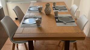 Una mesa de comedor lista con platos, tazas y una jofaina, rodeada de sillas.