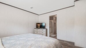A bedroom with a bed, a dresser, a television, and a door leading to a bathroom. - Redneck Riviera - Steinhatchee (Steinhatchee)