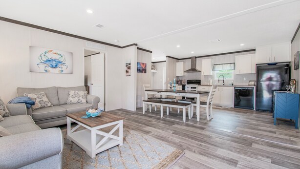 A modern living room with a sofa, coffee table, and a dining area with a table and chairs. There is a kitchen area with a refrigerator and a microwave. - Redneck Riviera - Steinhatchee (Steinhatchee)
