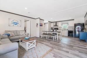 Una sala de estar moderna con un sofá, una mesa de centro y un comedor con una mesa y sillas. Hay una zona de cocina con un refrigerador y un microondas.