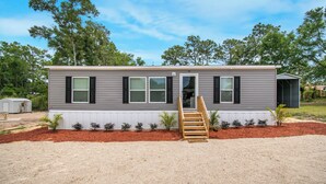 A single-story mobile home with a front entrance, a small porch, and a gravel driveway. - Redneck Riviera - Steinhatchee (Steinhatchee)