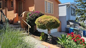 Una casa de dues plantes amb un porxo, un jardí petit amb diverses plantes i flors, i un garatge.