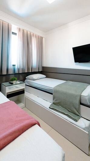 A modern hotel room with a bed, a desk, a television, and a window with curtains. - Cupe Beach Living Porto de Galinhas (Ipojuca)