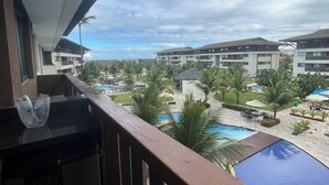 A balcony with a view of a resort pool area, including multiple swimming pools and palm trees. - Cupe Beach Living Porto de Galinhas (Ipojuca)