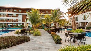 A hotel pool area with multiple levels of balconies, outdoor seating, and palm trees. - Cupe Beach Living Porto de Galinhas (Ipojuca)