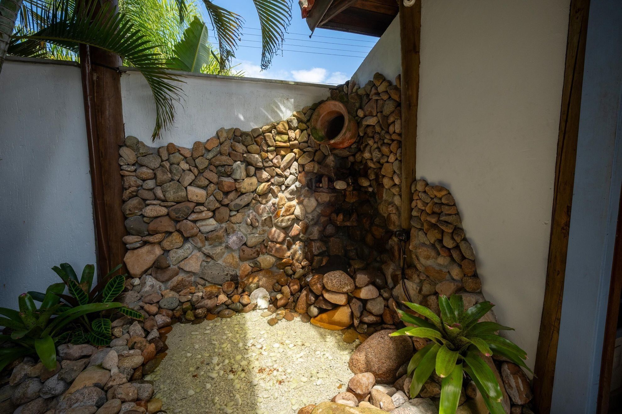 A stone wall with a circular opening, surrounded by rocks and plants.
