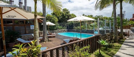 Una piscina al aire libre, sombrillas, sillones reclinables de piscina