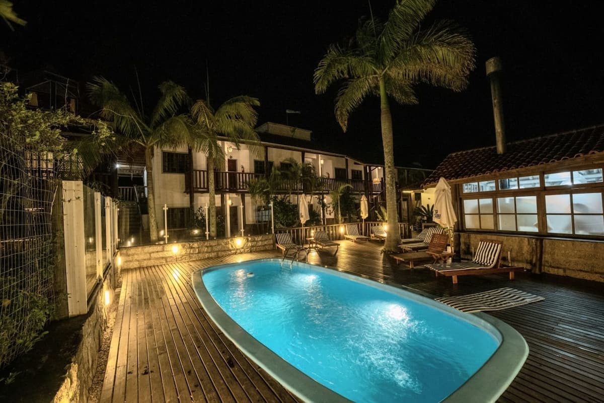 A swimming pool with lounge chairs and palm trees at night.