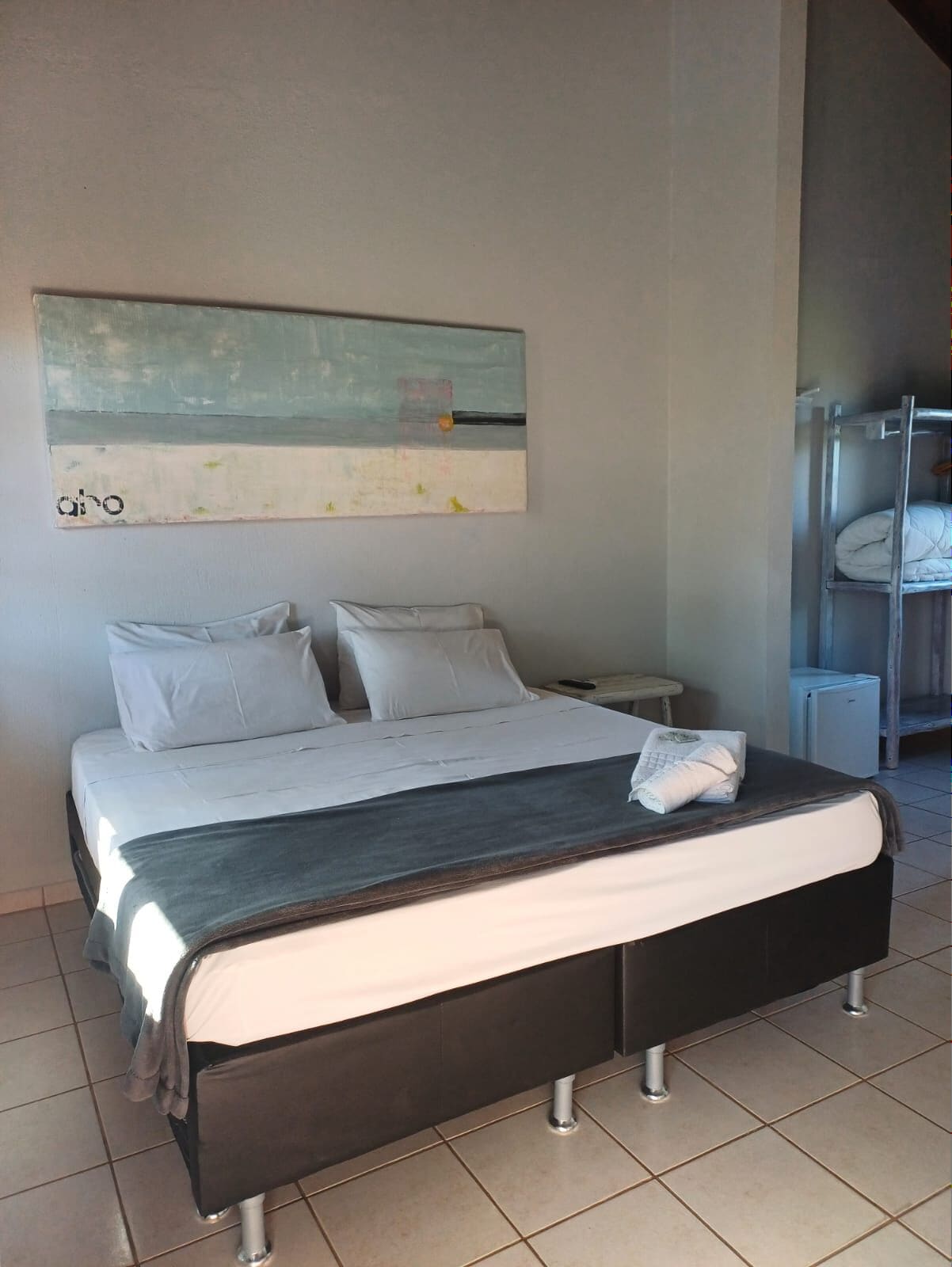 A modern hotel room with a large bed, a nightstand, a wall-mounted painting, and a bunk bed in the background.