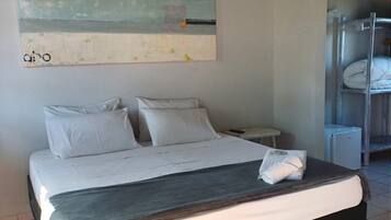 A modern hotel room with a large bed, a nightstand, a wall-mounted painting, and a bunk bed in the background.