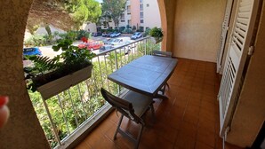 A balcony with a table and chairs, a view of parked cars, and greenery. - Beau Studio à 150 m de la mer Dans un Parc Privé ! (Six-Fours-les-Plages)