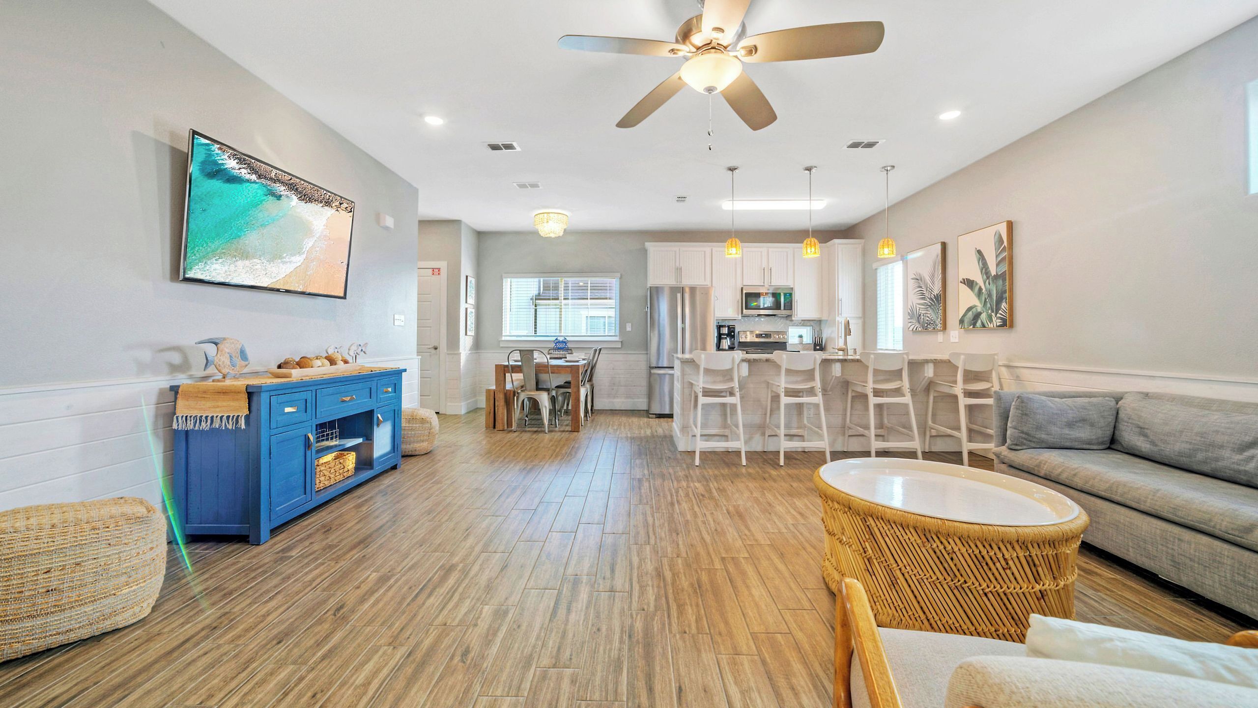 A modern living room with a sofa, a dining area, a kitchen, and a ceiling fan.