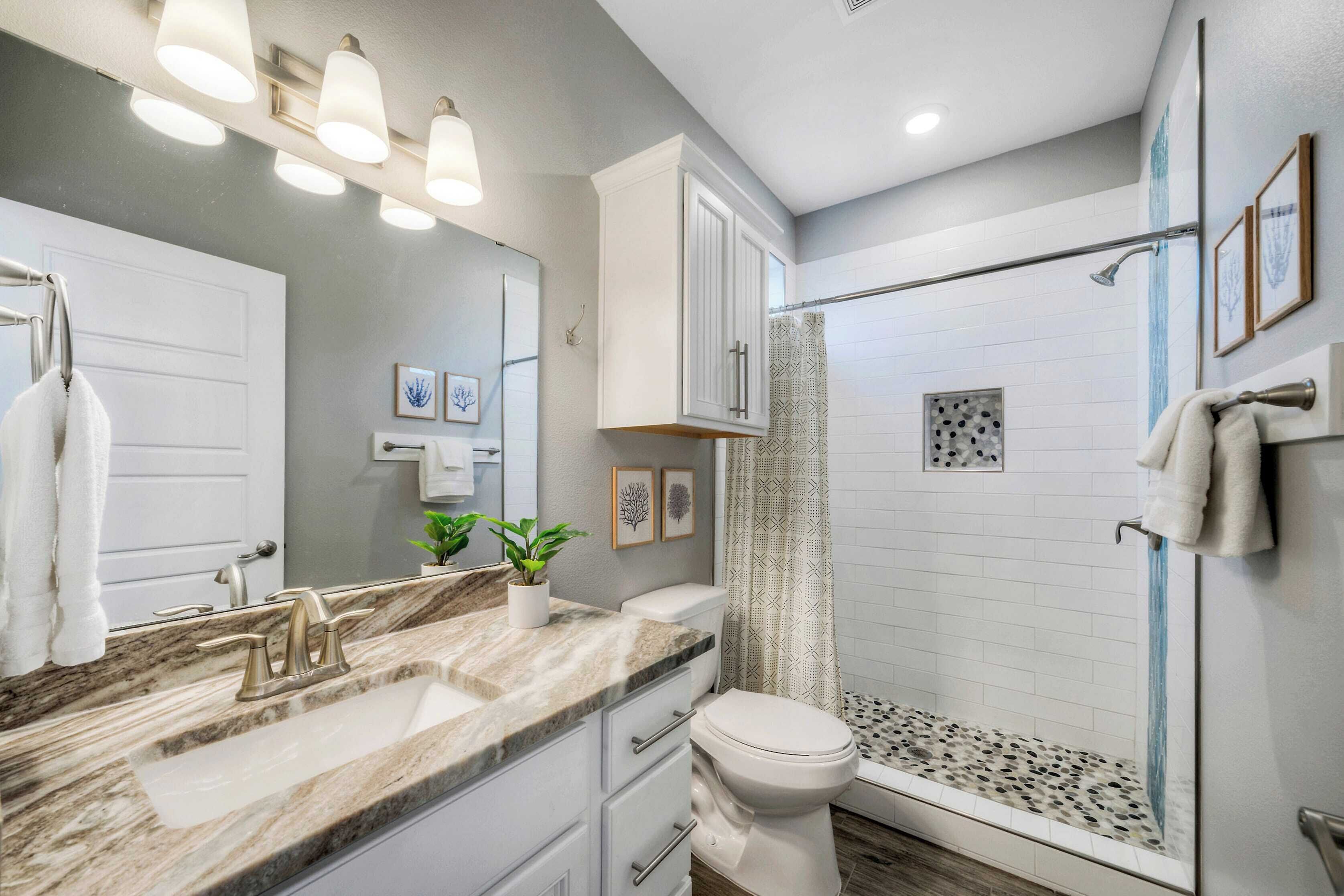 A modern bathroom with a marble sink, white cabinets, a glass shower enclosure, and a large mirror.