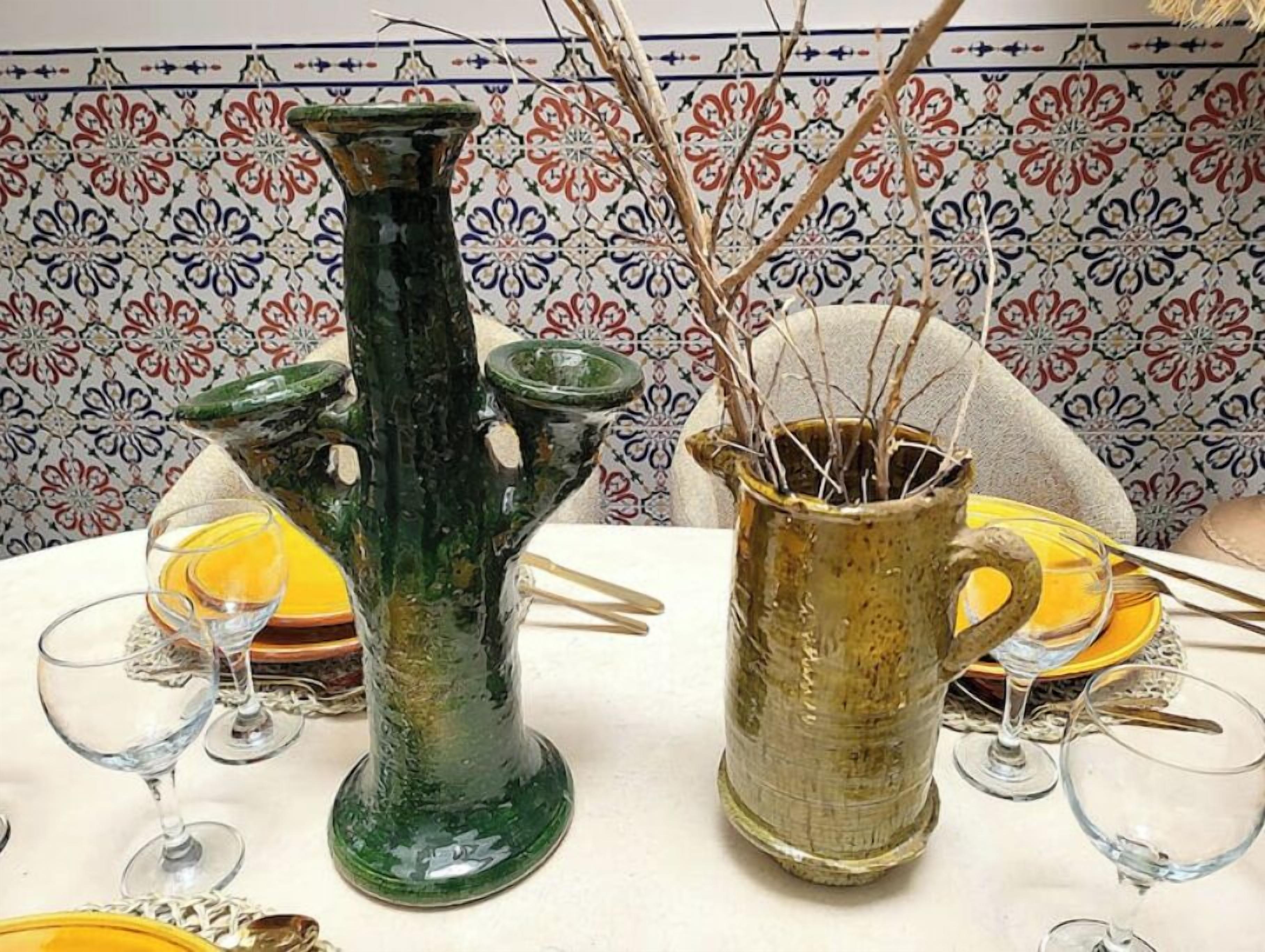 Una mesa dispuesta con un florero verde, una jarrón amarillo y copas de vino.