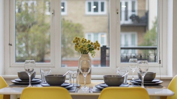 Une table à manger agrémentée de chaises jaunes, d’un vase de fleurs et de verres à vin.