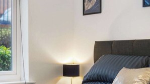 Un lit bien fait, avec des oreillers, une lampe de chevet et des œuvres d’art encadrées accrochées au mur.