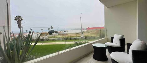 A balcony with a view of a green landscape and buildings, furnished with two chairs and a small table.