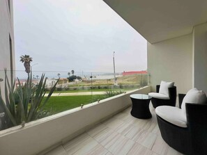 Un balcón con vistas a un paisaje verde y edificios, amueblado con dos sillas y una mesita.