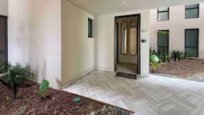 A modern building entrance with a tiled floor, a welcome mat, and a small garden area with plants and rocks. - Mision Viejo Sur 1BR Apartment B103 (Playas de Rosarito)