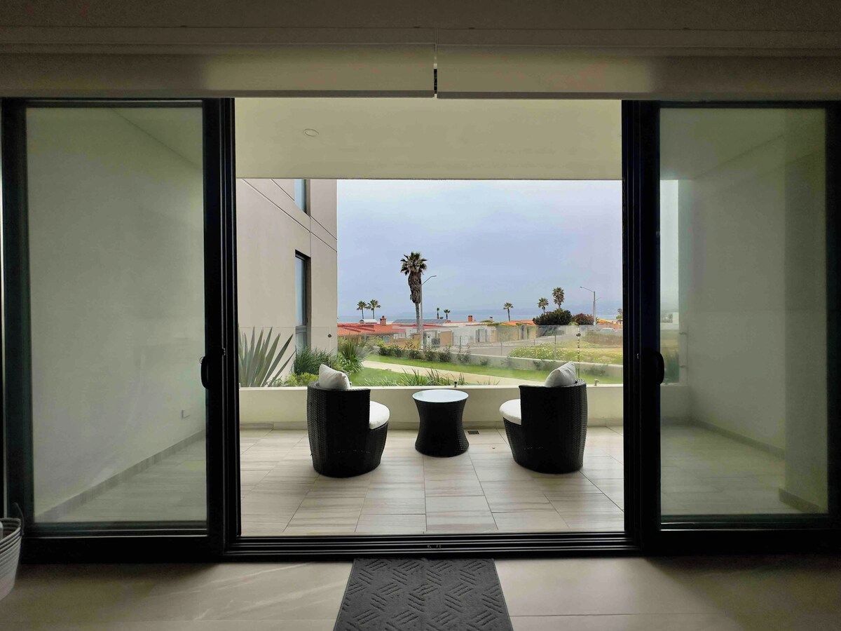 A room with a sliding glass door leading to an outdoor patio with two wicker chairs and a small round table.