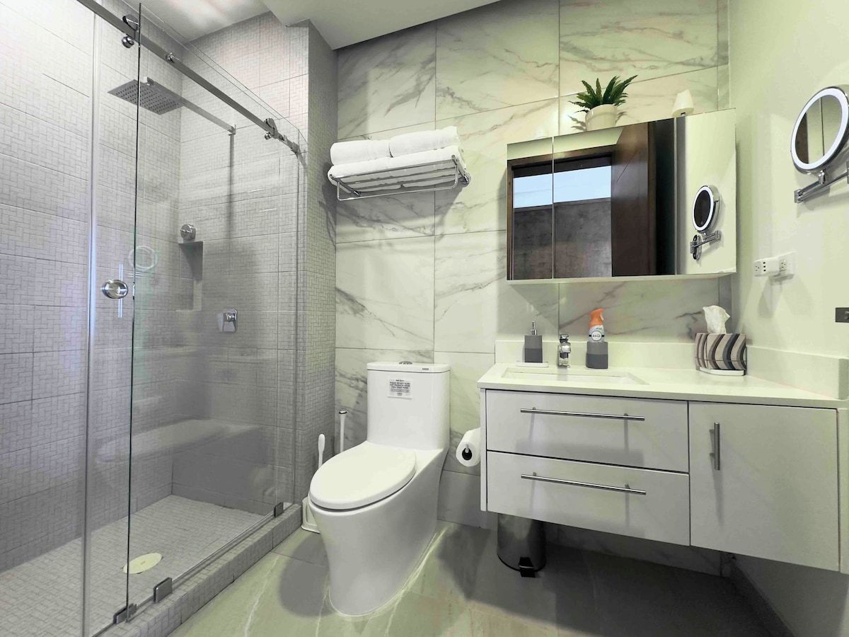 Un baño moderno con cabina de ducha de vidrio, inodoro, tocador con espejo y una pequeña planta en maceta.