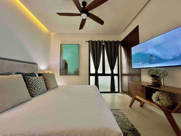 A modern bedroom with a large bed, a ceiling fan, a TV, and a window with curtains.