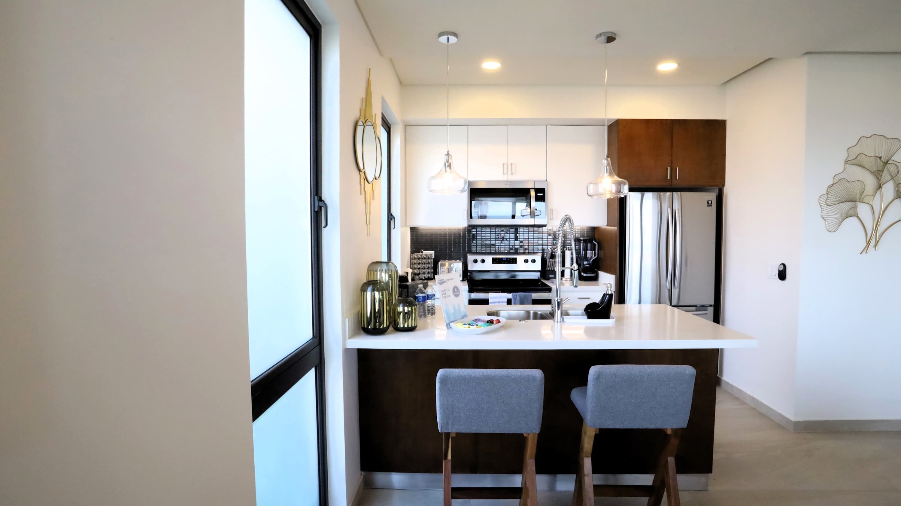 A modern kitchen with a central island, stainless steel appliances, and two grey chairs.