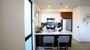 A modern kitchen with a central island, stainless steel appliances, and two grey chairs.