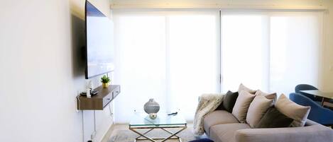 Un salon moderne avec un téléviseur à écran plat, une table basse en verre, un canapé et un fauteuil.