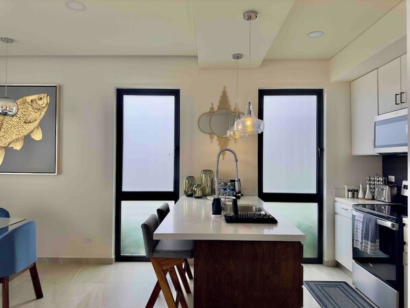 Una cocina moderna con una isla central, un área de comedor con una silla azul y una obra de arte de un pez grande en la pared.