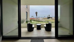 A modern room with a sliding glass door leading to an outdoor patio with three black wicker chairs and a small round table. - Mision Viejo Sur 1BR Apartment B103 (Playas de Rosarito)