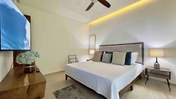 A modern bedroom with a large bed, a ceiling fan, a TV mounted on the wall, and a bedside table with a lamp.