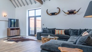 Una sala moderna con un sofá seccional gris, una mesa de centro de vidrio y una mesita de noche de madera. Hay un televisor montado en un mueble de madera y un ventanal que proporciona luz natural.