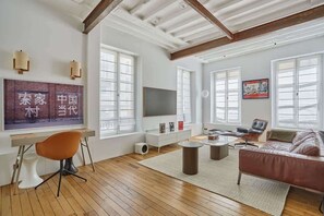Ein geräumiges Wohnzimmer mit Holzboden, einer Couch, einem Couchtisch, einem Fernseher und einem Schreibtisch mit Stuhl.