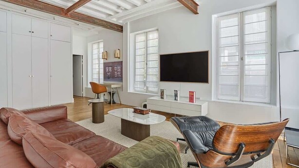 Un salon spacieux doté d’un grand téléviseur, de canapés en cuir, d’un fauteuil en bois et d’un coin repas avec une table et des chaises.