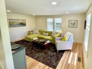 Una sala de estar con un sofá verde, un sillón gris y una alfombra estampada.