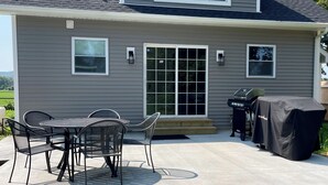 A two-story house with a covered patio area featuring a table and chairs, a grill, and a covered barbecue table. - Family home by Polo fields with great yard & game rm. EV charger, pet friendly! (Pine Plains)