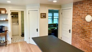 A kitchen with a long counter, a brick wall, and a view into a living area with a green couch. - Family home by Polo fields with great yard & game rm. EV charger, pet friendly! (Pine Plains)