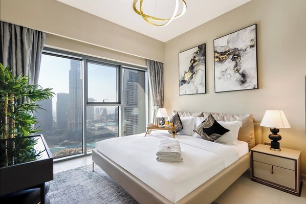 A modern hotel room with a large bed, two bedside tables, a nightstand, a potted plant, and a city view.