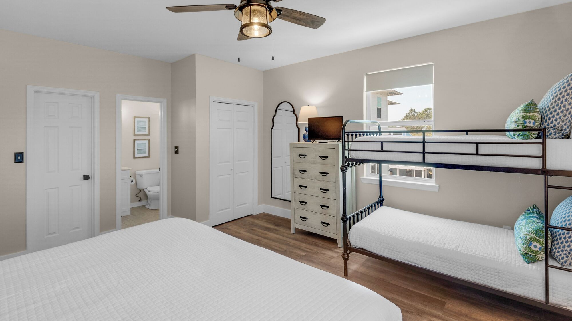A bedroom with bunk beds, a dresser, a ceiling fan, and a window with a view.