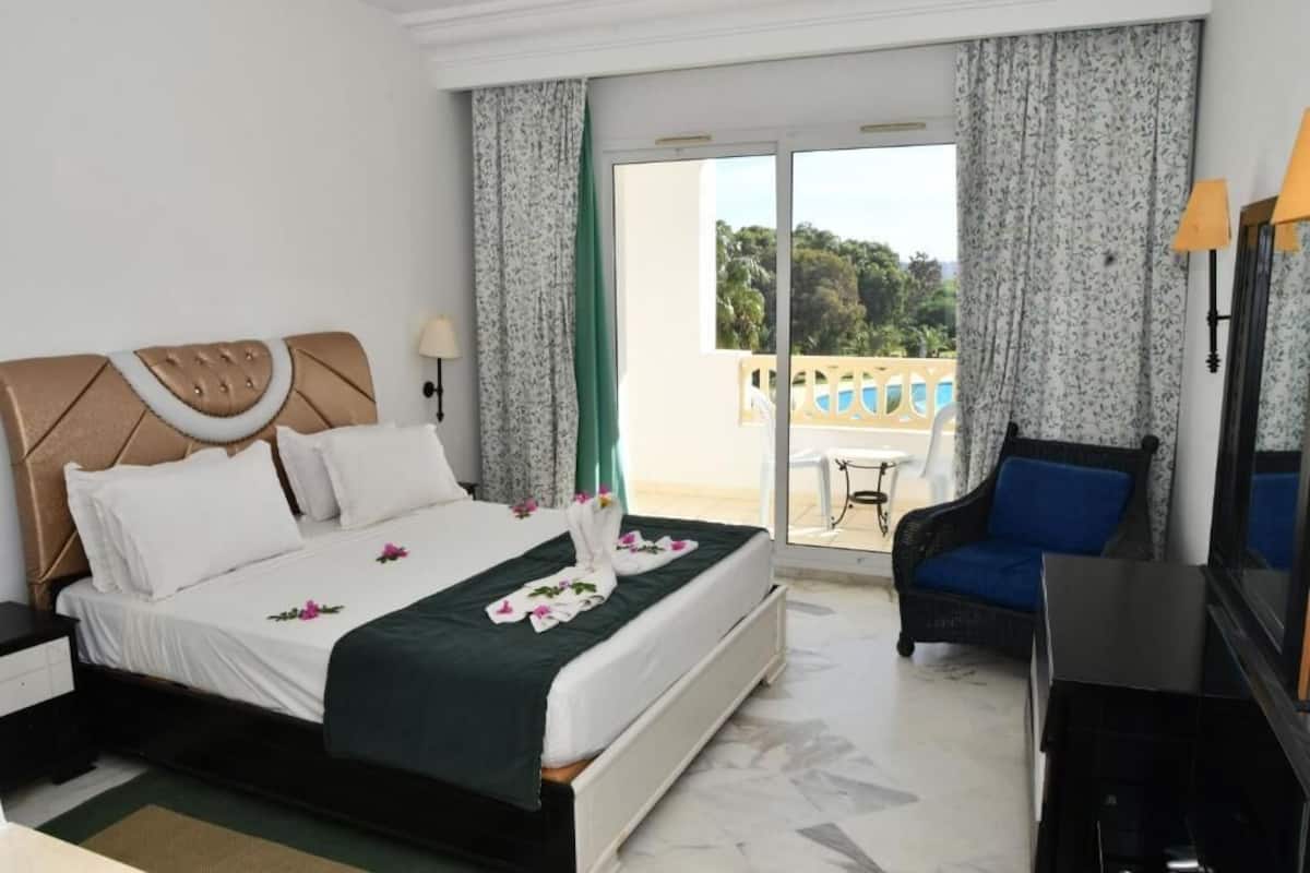A hotel room with a bed, a chair, a TV, and a balcony with a view.