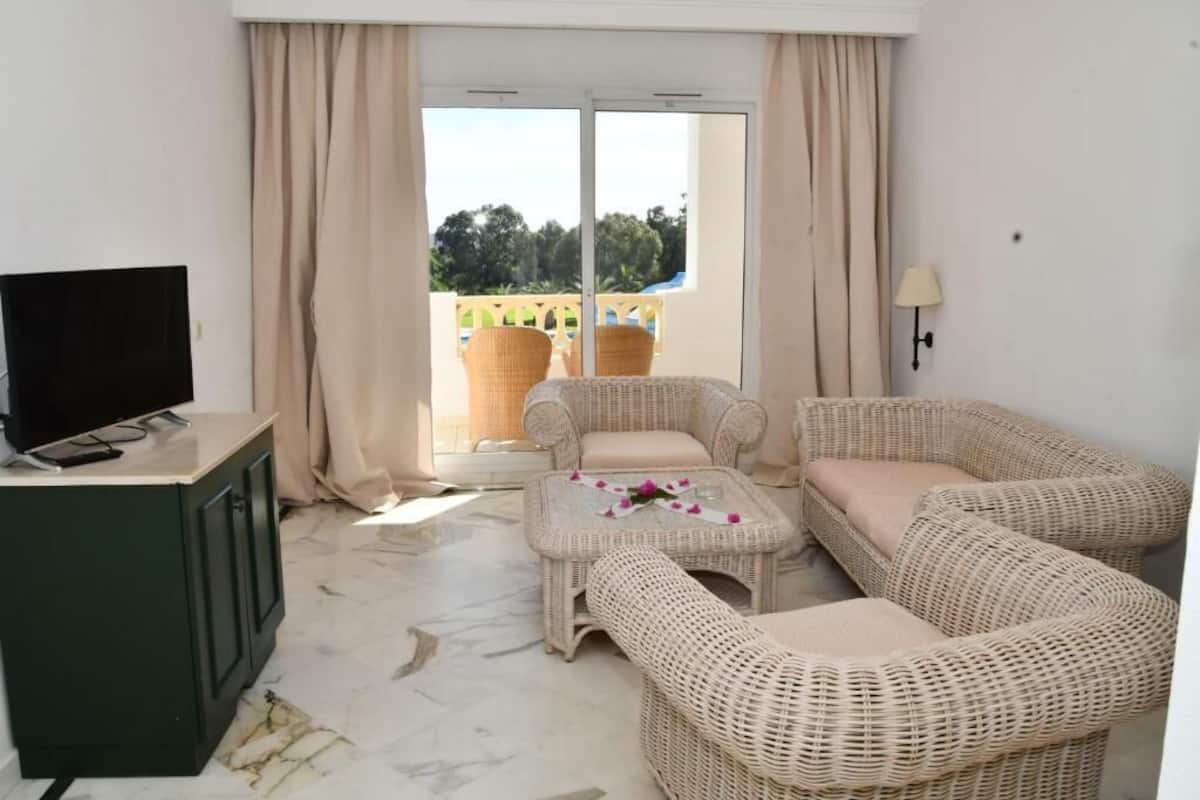 A living room with wicker furniture, a TV on a cabinet, and a view through a glass door.