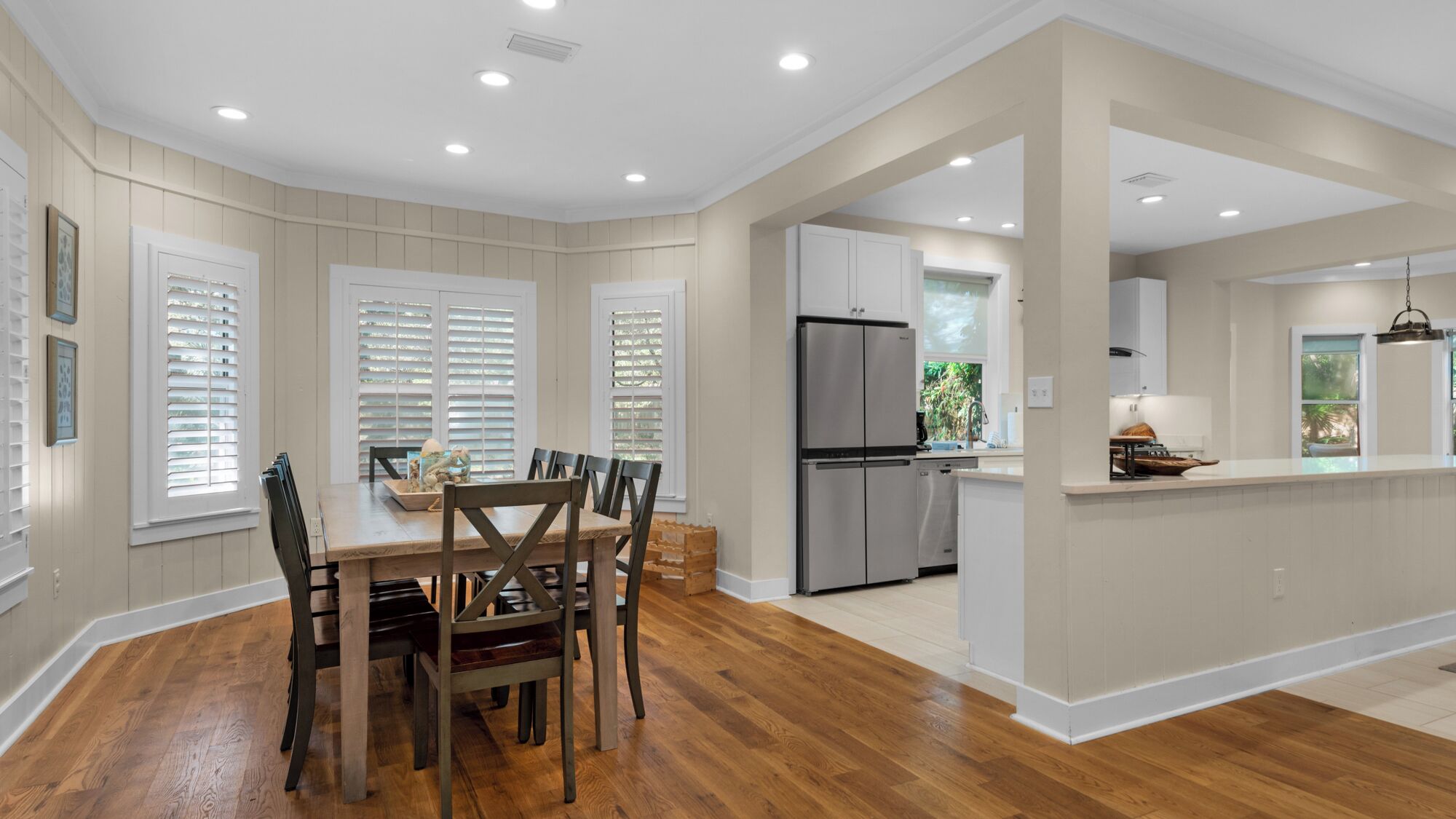 Una cocina moderna con armarios blancos, un refrigerador de acero inoxidable y una mesa de comedor de madera con sillas.