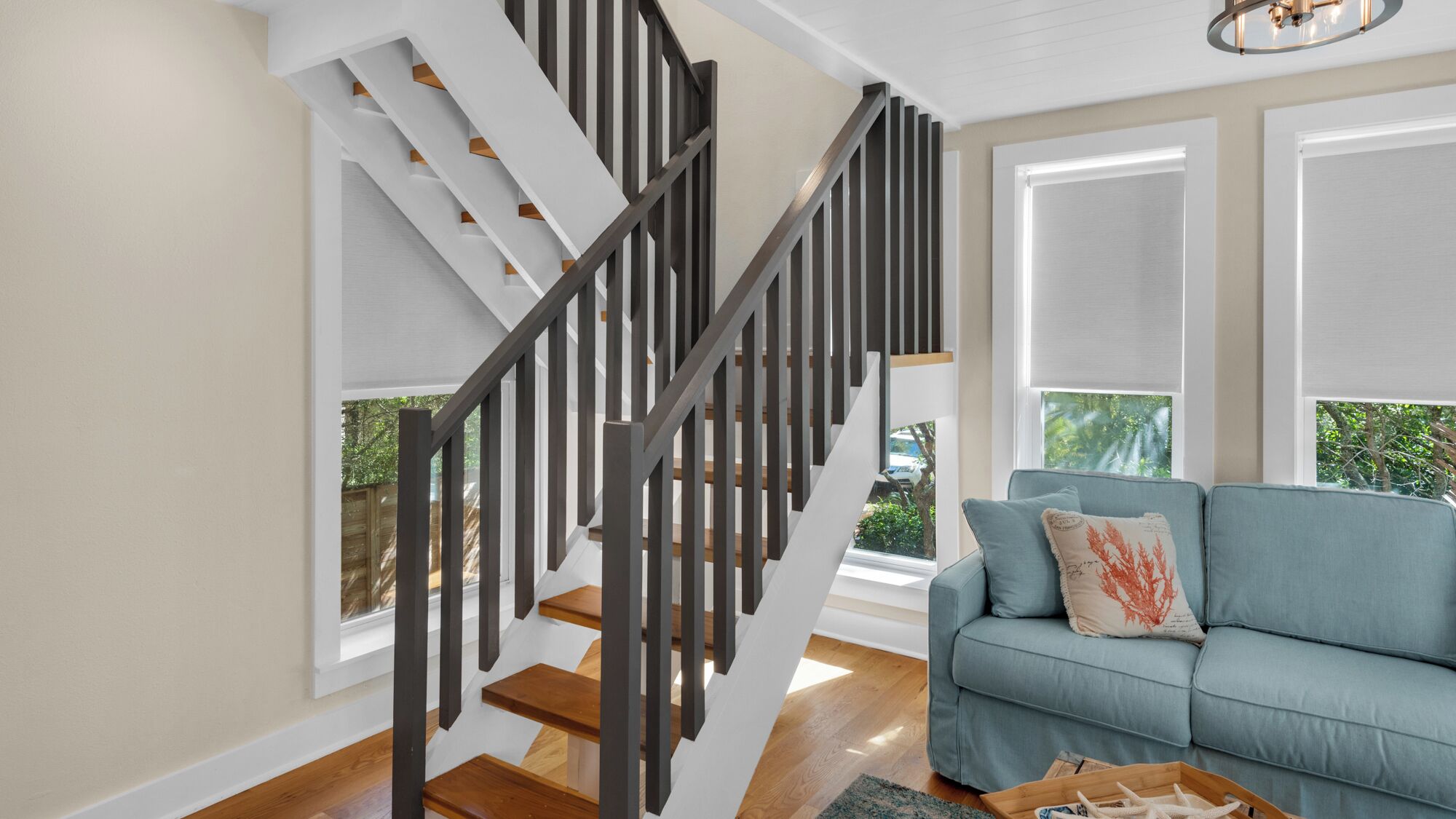 Una moderna scala con gradini in legno e ringhiere scure, che conduce a un divano azzurro chiaro con cuscini decorativi.