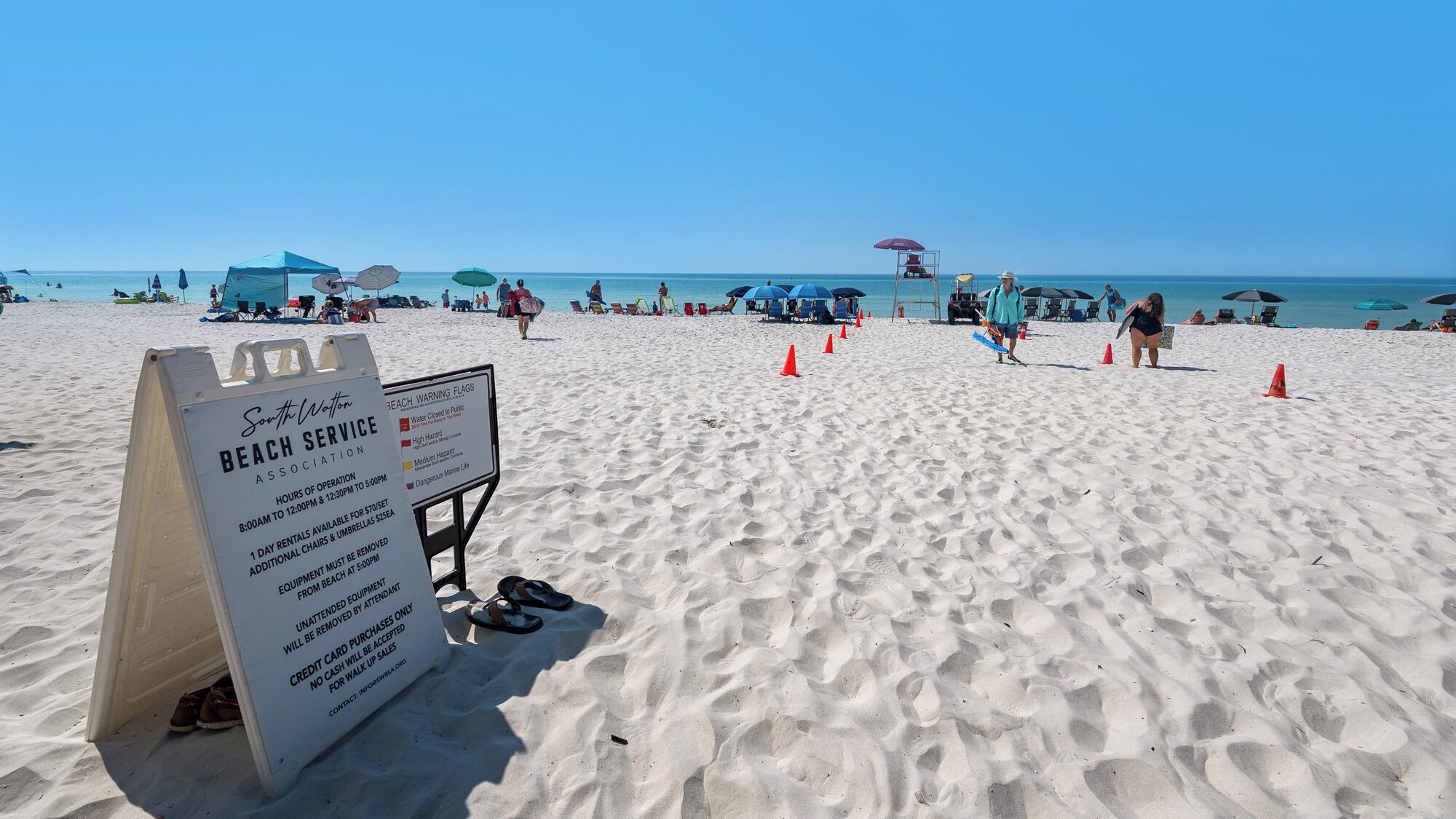 A beach with a sign detailing beach services, including hours of operation and rental information.