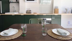 Moderni keittiö, jossa on mikroaaltouuni, leivänpaahdin ja pesuallas. Keittiössä on ruokapöytä, pöytäliinat ja viinilasi.